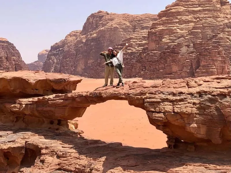 Jeep driving across open red desert in Wadi Rum, Jordan, with massive sandstone cliffs on the horizon during a flexible jeep tour