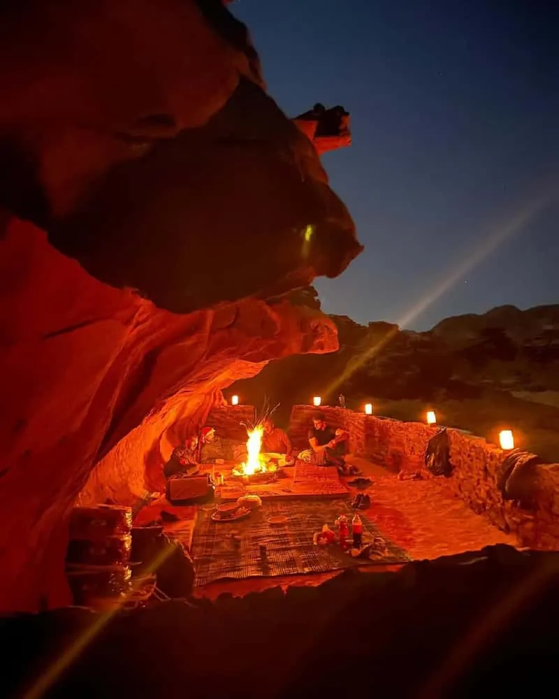 Stars and Milky Way visible over Wadi Rum desert at night, Bedouin camp fire glowing in the foreground during overnight jeep tour in Jordan