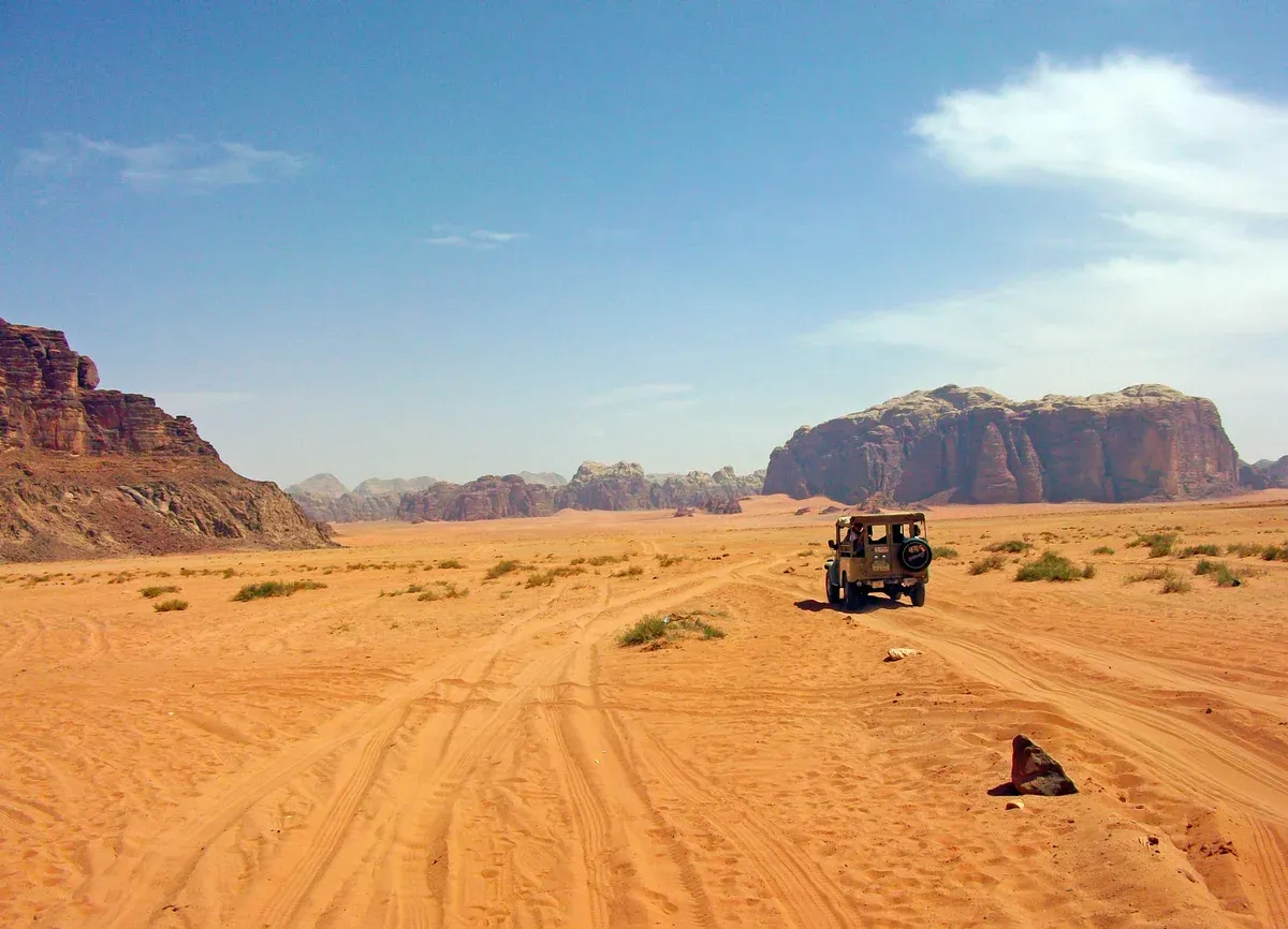 An open-back 4x4 jeep heading out across red sand toward the sandstone islands of Wadi Rum on a desert safari in Jordan